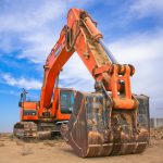 A large orange excavator working on a construction site under a blue sky.